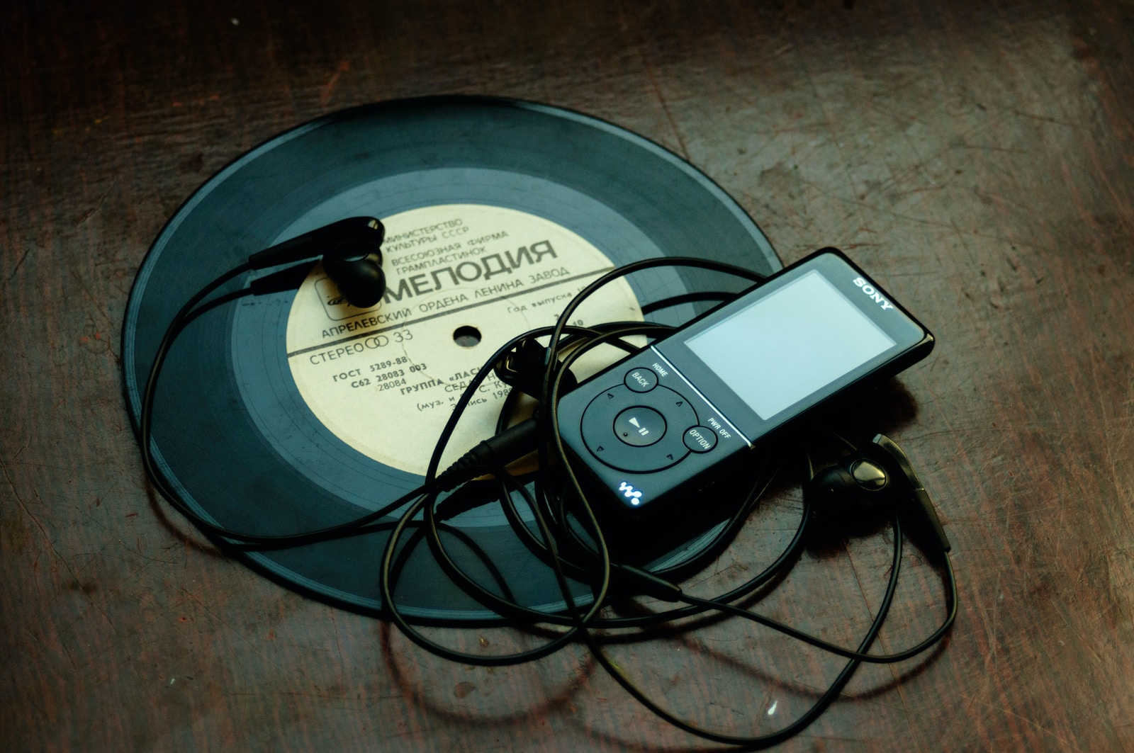 Des écouteurs intra-auriculaires branchés sur un baladeur Sony noir posé sur un disque vinyle