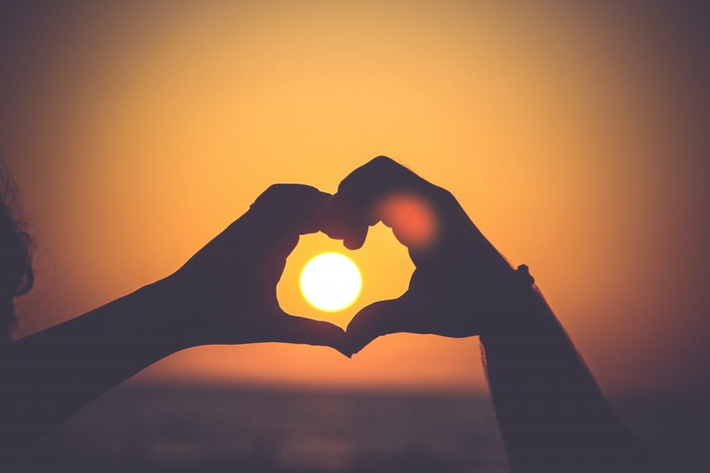 Une personne tient ses mains en forme de cœur devant le soleil